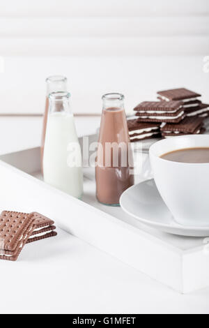 Tasse de café et quelques bouteilles de lait et chocolat lait frappé sur un plateau blanc sur fond blanc volets Banque D'Images