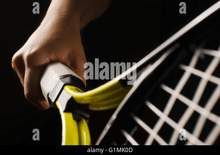 Main sur l'adhérence et balançant une raquette de tennis. Isolé sur fond noir. Banque D'Images