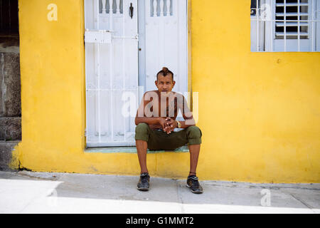 Un jeune homme avec tattoo est assis sur le seuil de la maison jaune à Santiago de Cuba, Cuba. Banque D'Images