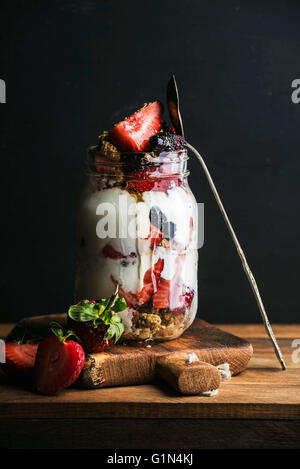 L'avoine yaourt muesli aux fraises, mûres, le miel et les feuilles de menthe en grand pot du verre sur fond noir Banque D'Images