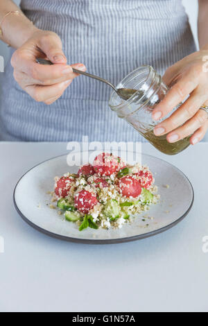 Une femme gettitng est prêt à arroser une pastèque salade de boulgour au citron vert et miel vinaigrette. Banque D'Images