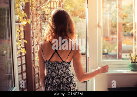 Une jeune femme est debout sur le seuil de sa cuisine et il se penche sur le jardin au lever du soleil Banque D'Images