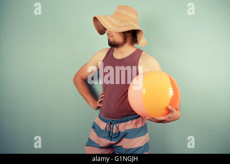Un jeune homme portant un chapeau de soleil est holding beach ball Banque D'Images