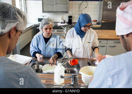 Classe internationale pendant la cuisson d'un gâteau dans la cuisine de l'école. Les stagiaires se laver les ustensiles de cuisine. Banque D'Images