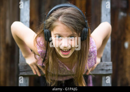 Petite fille espiègle émotionnelle avec casque, close-up portrait en extérieur. Banque D'Images