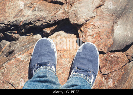 Les pieds mâles bleu chaussures de sport en toile permanent sur un sol rocailleux Banque D'Images