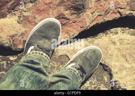 Les pieds mâles en toile de jeans et chaussures debout sur un sol rocailleux, correction tonale chaud vintage effet filtre photo, style ancien Banque D'Images