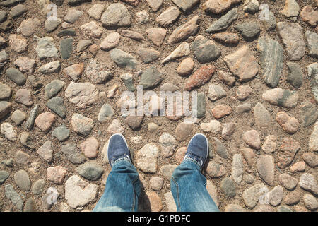 Les pieds mâles en blue-jeans et baskets sur la vieille chaussée de pierre rugueuse Banque D'Images