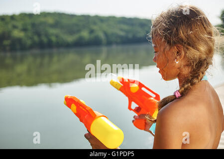 Jeune fille jouant avec un fusil sur un lac squirt sur les vacances d'été Banque D'Images