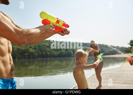 Famille à un lac à pulvériser de l'eau à l'autre avec un fusil et squirt s'amusant en été Banque D'Images