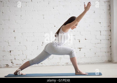 Attractive young woman working out à l'intérieur. Beau modèle de faire les exercices sur tapis bleu dans la pièce avec des murs blancs Banque D'Images