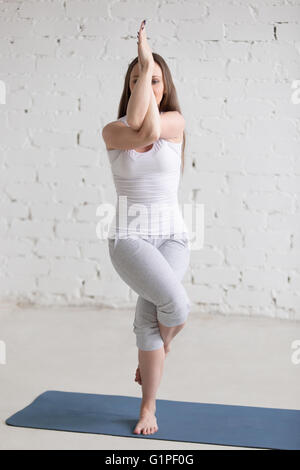 Attractive young woman working out à l'intérieur. Beau modèle de faire les exercices sur tapis bleu dans la pièce aux murs blancs. Posture de l'aigle Banque D'Images