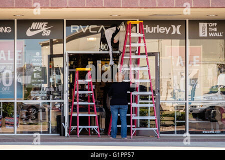 Une femme de race blanche les plans tremblotants d'une échelle alors qu'un homme un signe de bandes d'une vitrine de magasin. Oklahoma City, Oklahoma, USA. Banque D'Images