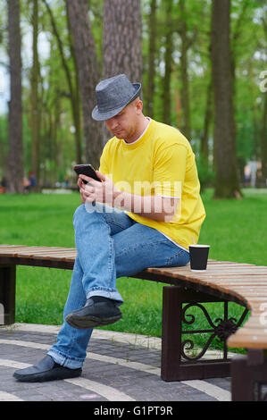 Homme est assis sur un banc dans le parc avec le smartphone Banque D'Images