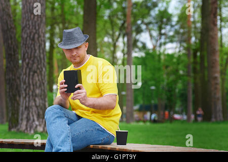 Homme est assis sur un banc dans le parc avec le smartphone Banque D'Images