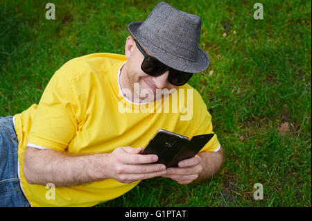 Jeune homme intelligent dans un T-shirt jaune avec le téléphone sur l'herbe Banque D'Images