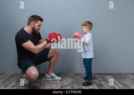 Père et petit fils jouant dans des gants de boxe ensemble sur fond gris Banque D'Images