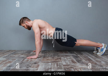 Jeune homme barbu attrayant faisant push-ups sur fond gris Banque D'Images