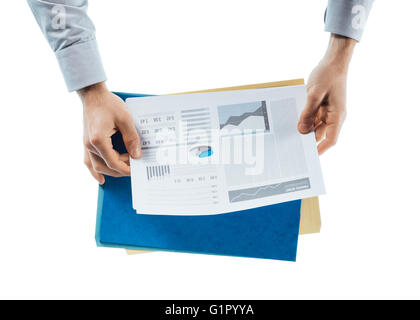 Businessman reading un rapport financier avec des tableaux et graphiques sur fond blanc, les mains de près, vue de dessus Banque D'Images