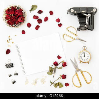 Mise à plat avec album photo, pétales de rose rouge, vintage camera, ciseaux sur fond blanc. Maquette sketchbook fleurs Banque D'Images