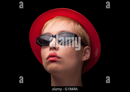 Vue avant horizontale portrait d'une jeune femme blonde avec Red Hat et lunettes noires sur fond noir Banque D'Images