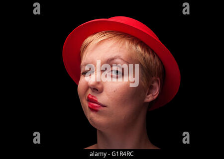 Vue avant horizontale portrait d'une jeune femme blonde avec red hat faisant un visage sur fond noir Banque D'Images