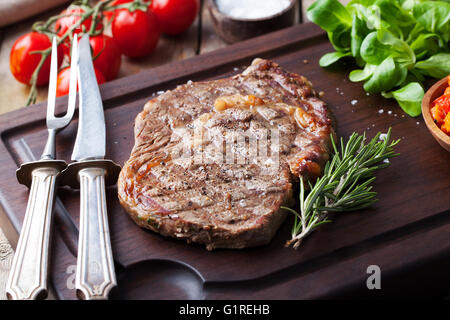 Pavé de boeuf avec tomates cerises et romarin sur un fond de bois à découper. Banque D'Images