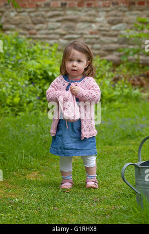 Tout-petit debout dans jardin avec le cardigan tricoté Banque D'Images