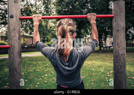 Une jeune femme est en train de faire pullups dans le parc Banque D'Images