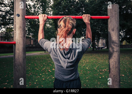 Une jeune femme est en train de faire pullups dans le parc Banque D'Images