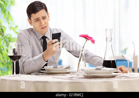 Déçu jeune homme assis à une table de restaurant et la lecture d'un message texte sur sa cellule Banque D'Images