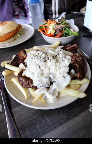 Une assiette de steak avec une sauce aux champignons et frites avec un bol de salade grecque dans l'arrière-plan Banque D'Images