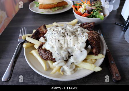 Une assiette de steak avec une sauce aux champignons et frites avec un bol de salade grecque et poulet Schnitzel burger dans l'arrière-plan Banque D'Images