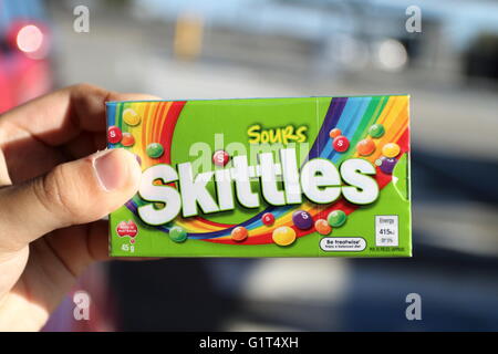 Close up of hand holding fort de bonbons Skittles sour dans emballage vert Banque D'Images