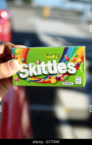 Close up of hand holding fort de bonbons Skittles sour dans emballage vert Banque D'Images