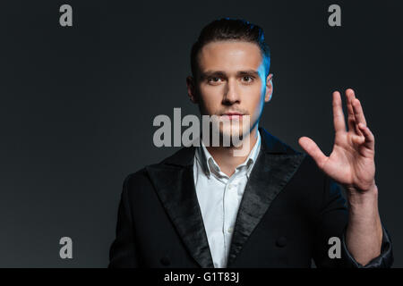 Portrait of young man magicien avec main levée sur fond gris Banque D'Images