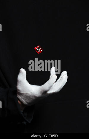 Main de l'homme magicien en gant blanc montrant à l'aide de l'un des astuces sur fond noir dés de vol Banque D'Images