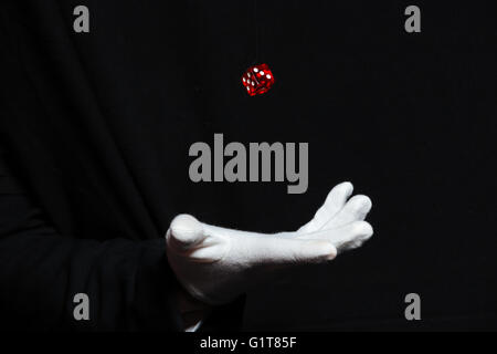 Main de l'homme magicien en gant blanc montrant les figures avec dés volant dans les airs sur fond noir Banque D'Images