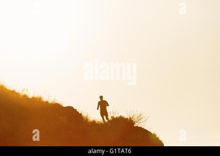 Silhouette d'un homme qui court sur la colline au coucher du soleil Banque D'Images