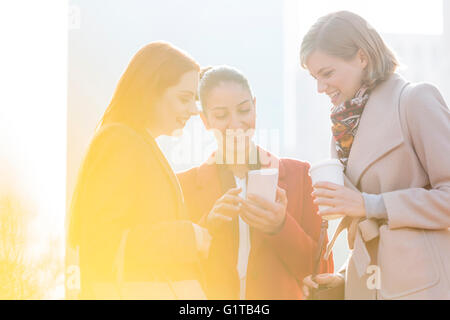 Smiling businesswomen texting et boire du café en plein air Banque D'Images