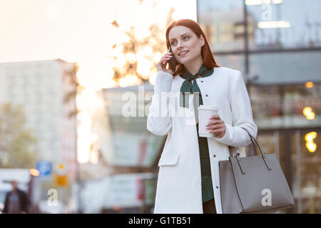 Businesswoman with coffee talking on cell phone in city Banque D'Images