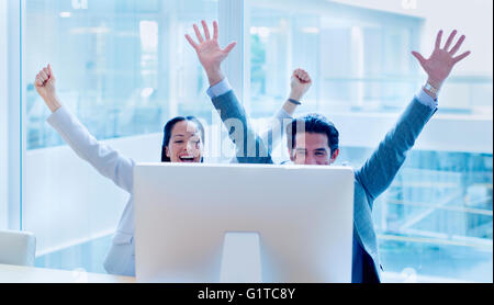 Exubérant businessman and businesswoman cheering with arms raised at computer in office Banque D'Images