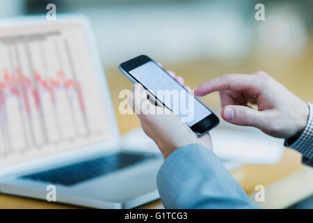 Close up of woman dialing cell phone at laptop Banque D'Images