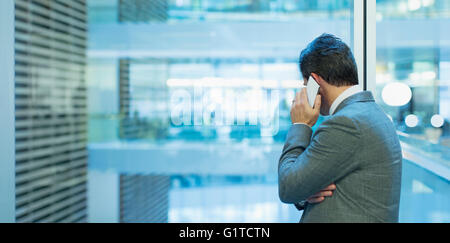 Businessman talking on cell phone at office window Banque D'Images