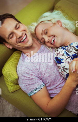 Rire affectueux couple laying on sofa with eyes closed Banque D'Images