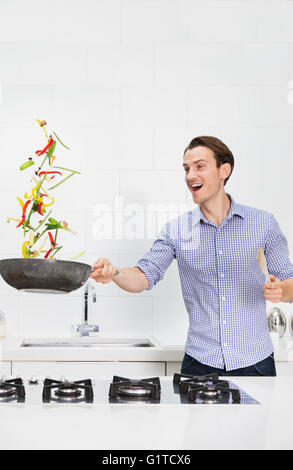 Surpris couple cooking et tourner les légumes dans la poêle dans la cuisine Banque D'Images