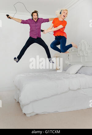 Portrait playful couple jumping on lit et écouter de la musique avec un lecteur mp3 et casque Banque D'Images