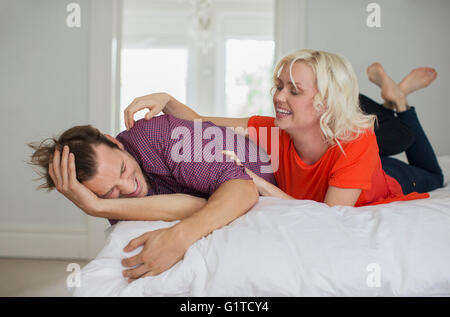 Femme espiègle chatouillant mari on bed Banque D'Images