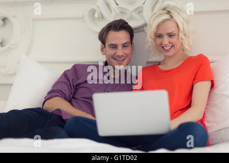Smiling couple using laptop on bed Banque D'Images