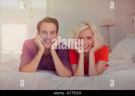 Portrait of smiling woman with head in hands on bed Banque D'Images